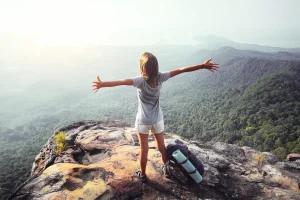 Young woman standing on cliff with arms raised in the air